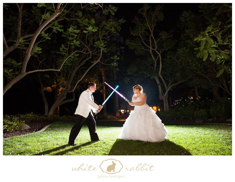A couple poses with lightsabers in front of the Disneyland Hotel in a dramatic Star Wars themed wedding photo.