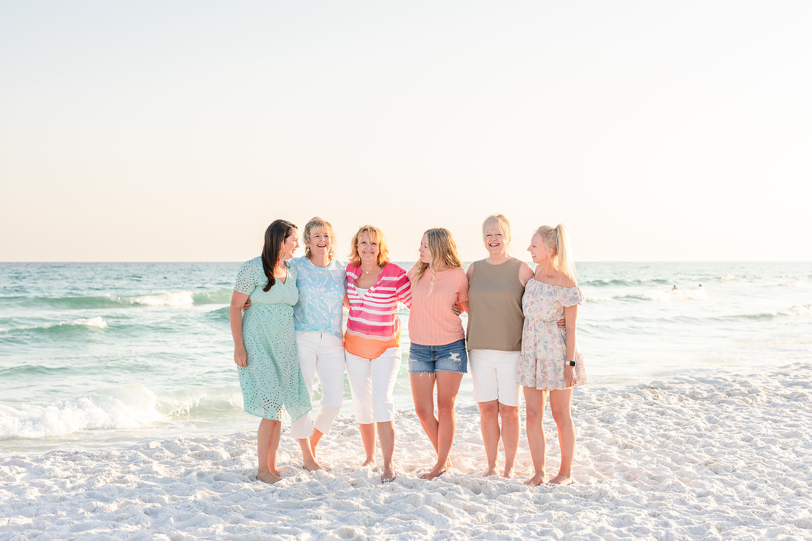 alt text: A family poses on the beach, with some members wearing floral prints that complement the solid colors worn by others.