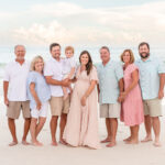 alt text: A family in coordinating blue and white outfits poses on the beach at sunset.