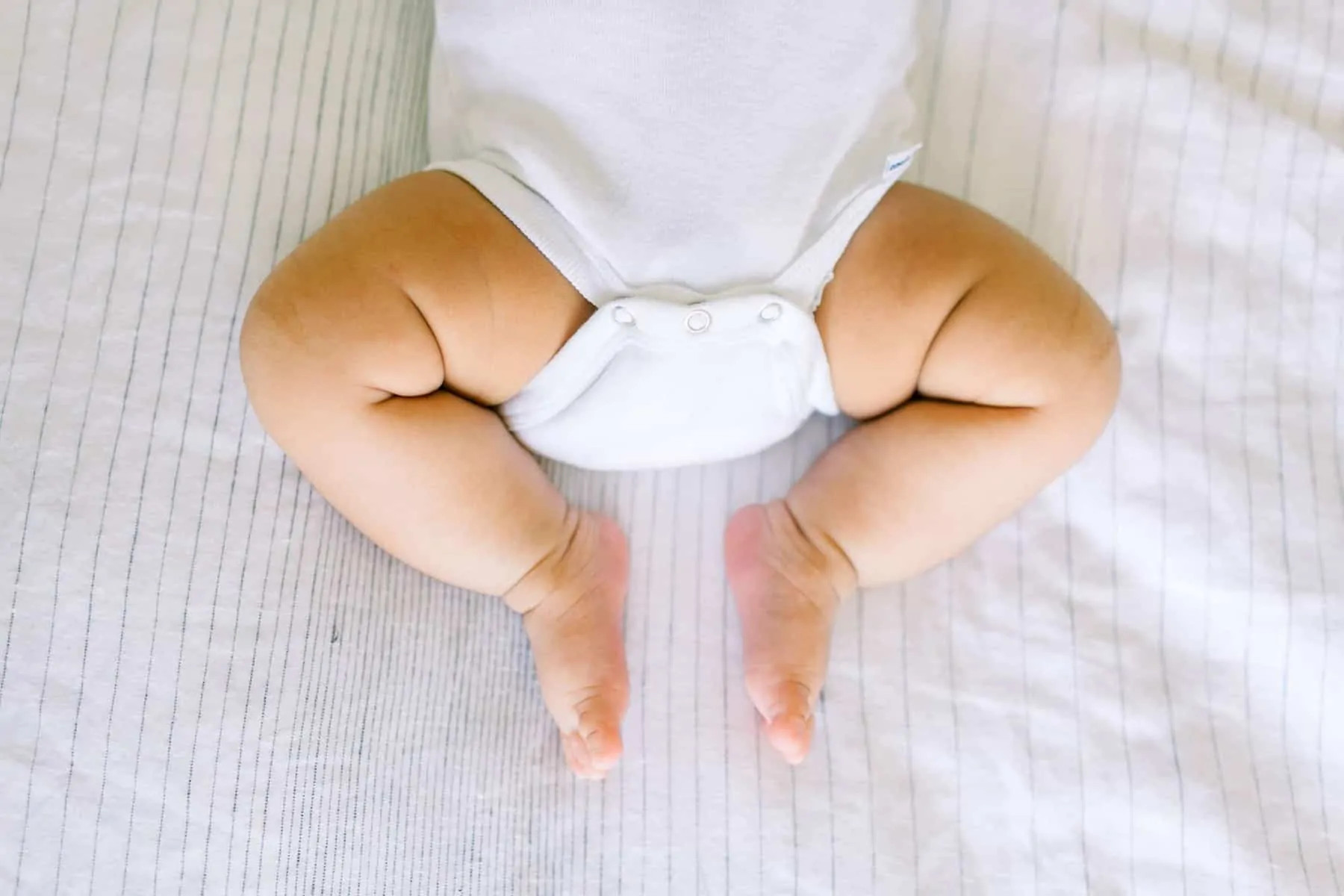 alt text: A baby laying on a bed with window light.