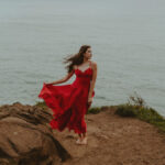 Senior girl in red dress standing on cliffside on the Oregon coast