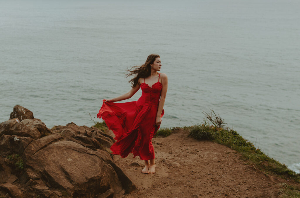 Senior girl in red dress standing on cliffside on the Oregon coast