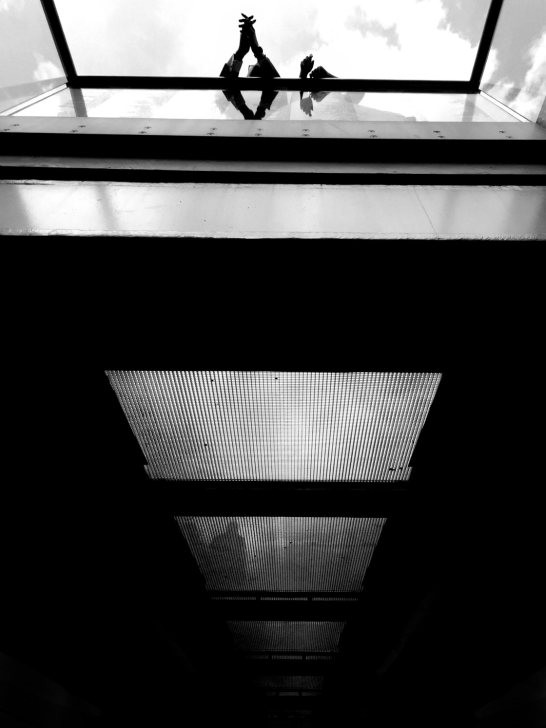 Black and white photograph in a train station, highlighting lines, shadows, and human activity