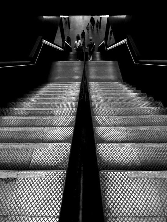 Black and white image of a solitary figure in a train station, captured waiting on a platform