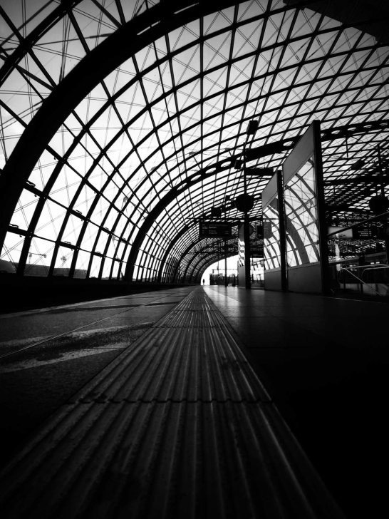 Black and white scene inside a train station, focusing on architectural details and waiting passengers