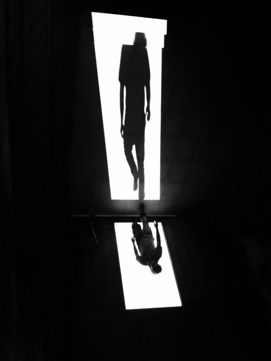 Dramatic black and white silhouette of a person against a brightly lit doorway, emphasizing shadow play