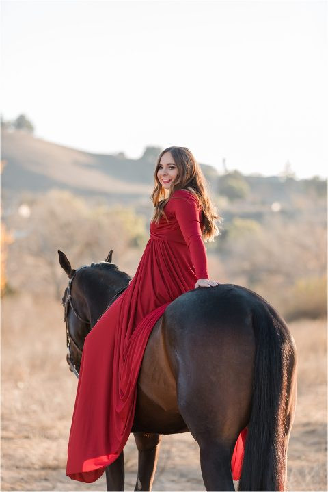 A horse photo of a woman in a flowing red dress with a dark horse at sunrise.
