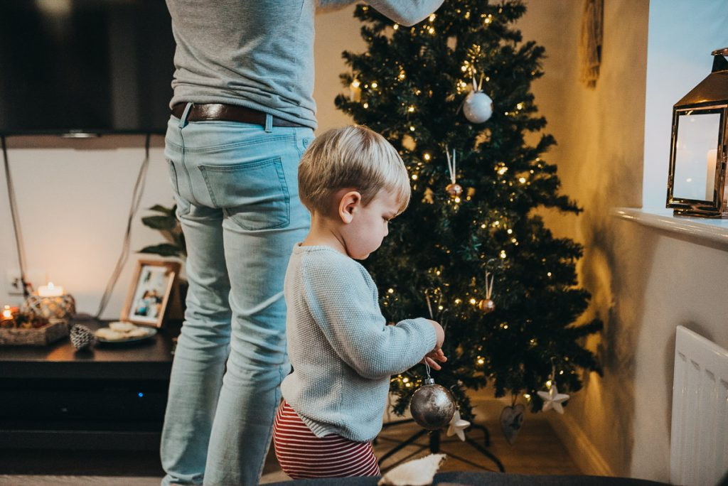 A child in a festive setting, looking at Christmas decorations, highlighting the importance of taking time to find the best angle and lighting for DIY Christmas photos.
