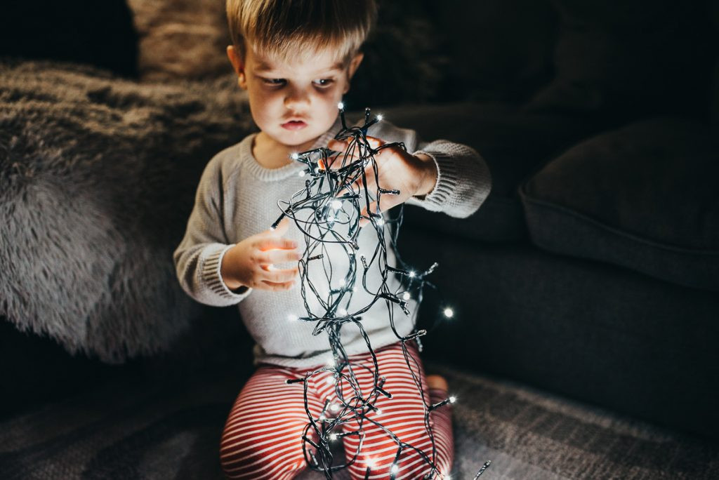 A child is playfully holding Christmas lights, demonstrating how lights can be used as props in DIY Christmas photos.