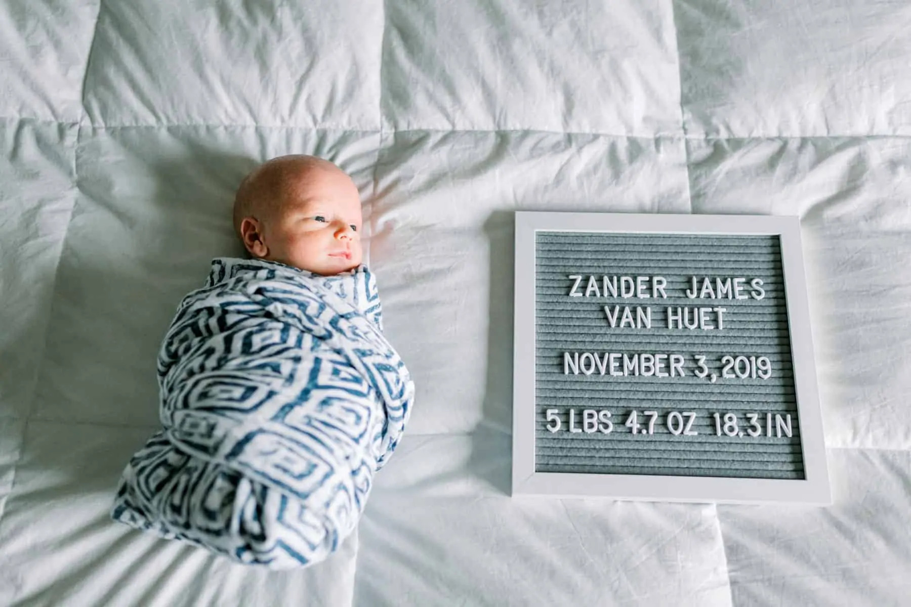 alt text: Overhead shot of swaddled baby on bed with letterboard.