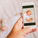 Mother taking a photograph on a smartphone of her newborn baby daughter