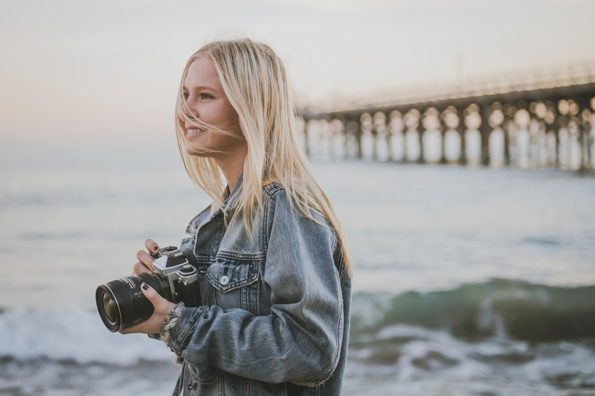 photographer by the shore holding a DSLR, looking off-camera and smiling