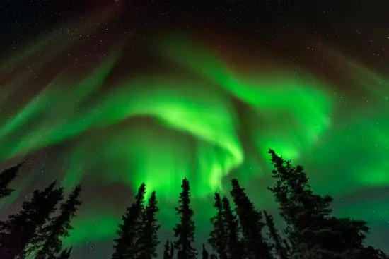 Photographer setting up a carbon fiber tripod in a snowy landscape under the northern lights, emphasizing stability for long exposures.