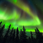 Northern lights display in Alaska, showcasing vibrant green and purple hues dancing across the night sky.