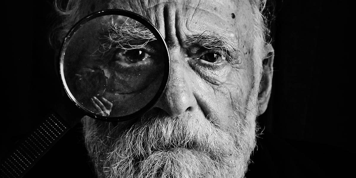 A close-up portrait of an elderly man with a magnifying glass, demonstrating filling the frame with the subject