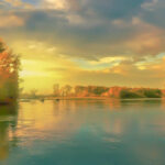 Alt text: A landscape photo of a lake and mountains at sunset, edited to look like a painting.