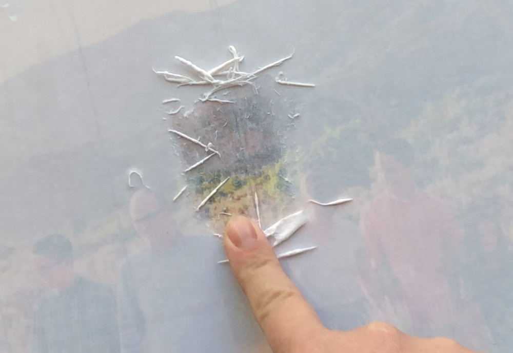 A finger gently rubbing wet paper fibers to reveal the photo image underneath during the transfer process.