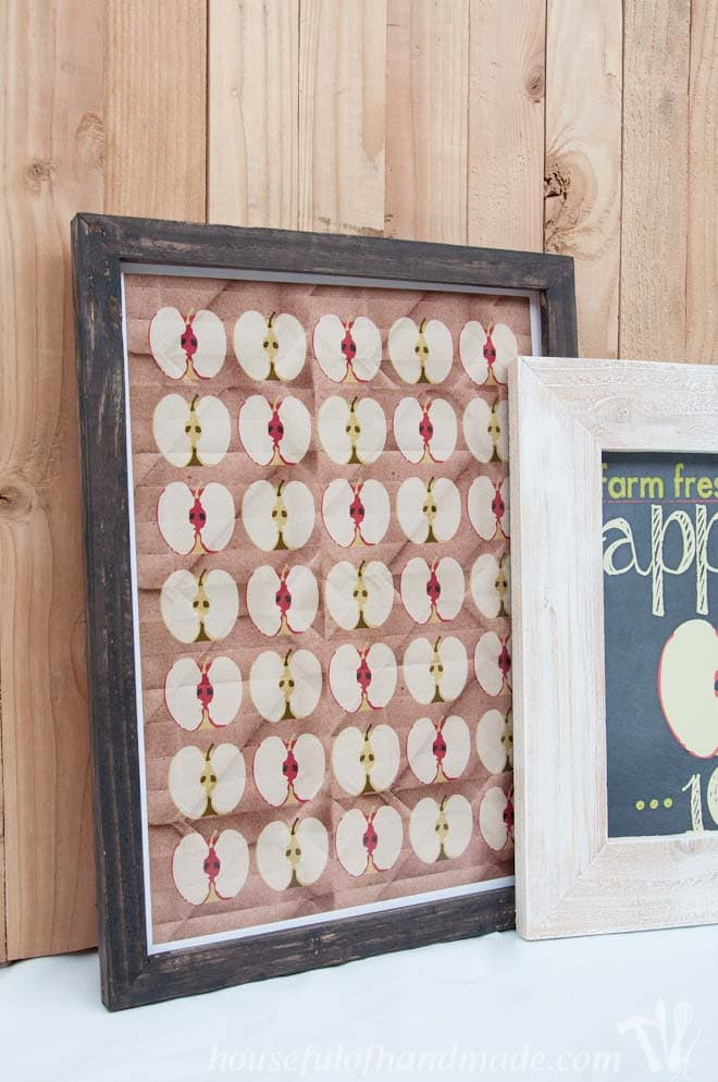 Two DIY rustic picture frames with apple printables displayed on a mantel, showcasing the completed fall-themed decor.