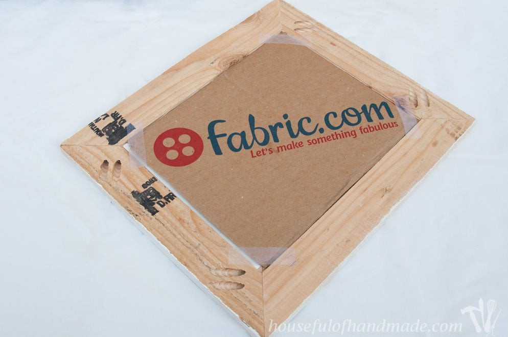 The back of a DIY rustic picture frame showing fabric.com cardboard taped as backing, a simple method for securing photos.