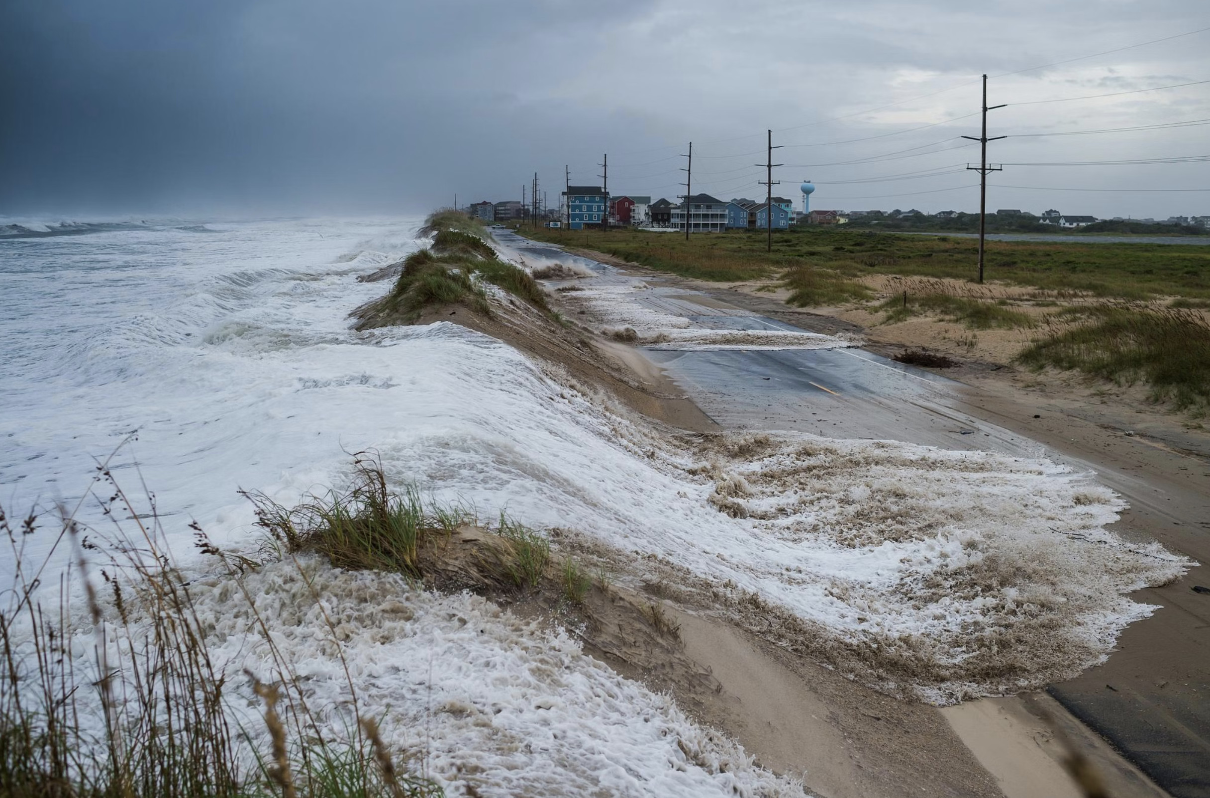 alt text: A color photo of a beach house with the ocean encroaching on its foundation.