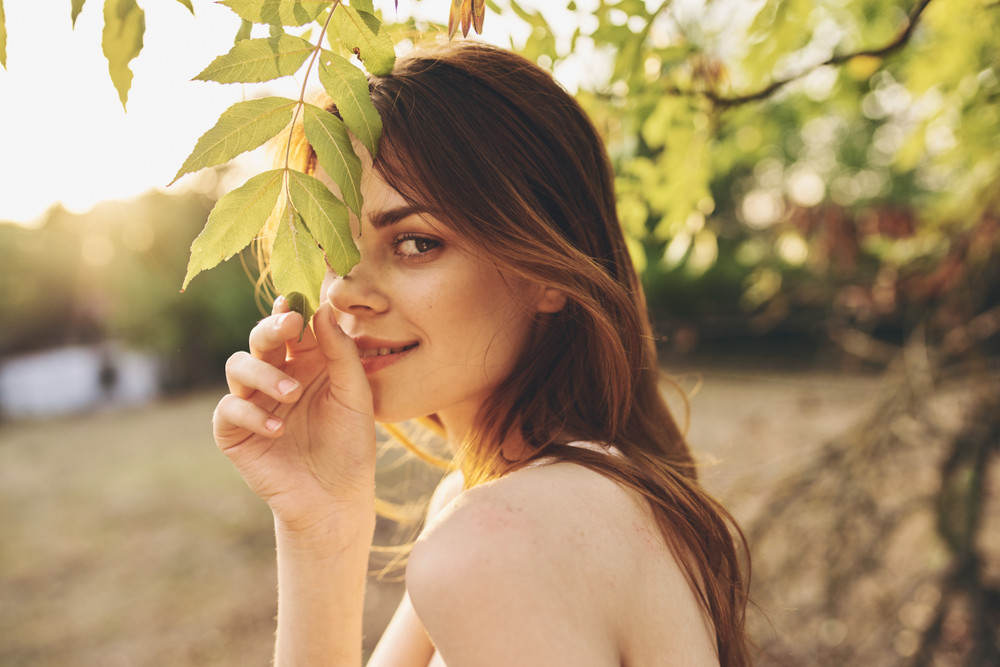 Woman in nature holding autumn leaves with serene expression