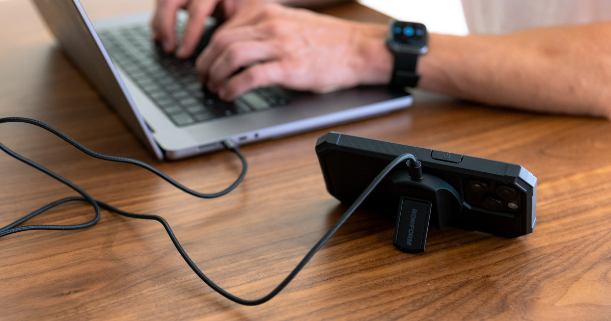 A person working on a laptop with an iPhone charging next to it, symbolizing data transfer and device management.