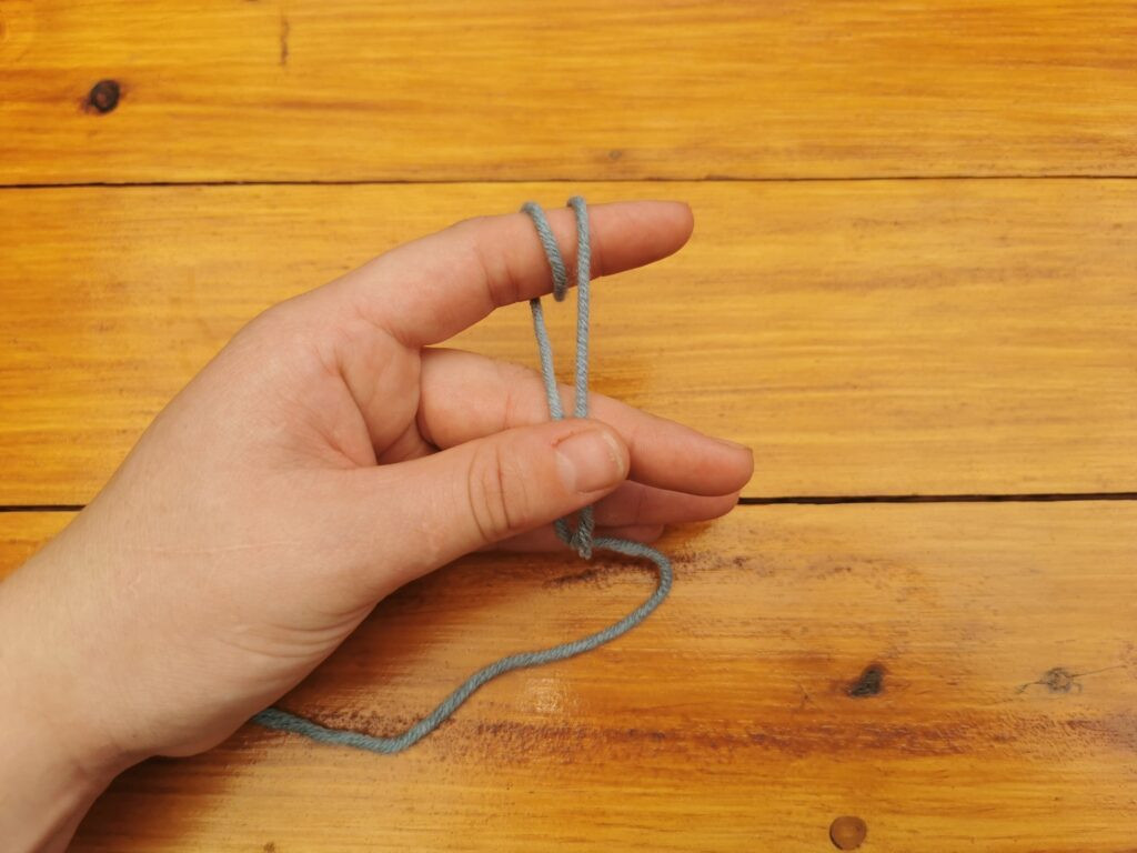 Holding both yarn ends stabilizes the loops, essential for tightening the slip knot correctly