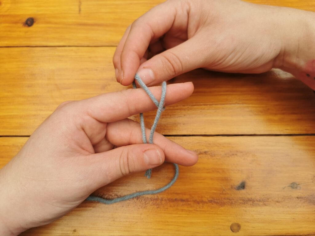 Pulling the back loop over the front loop begins to form the knot that secures the yarn