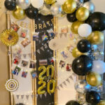 Graduation photo display screen with colorful crepe paper background, fairy lights, and balloon garland