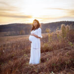 Expecting mother in white dress in golden field, first baby, captured at 34 weeks
