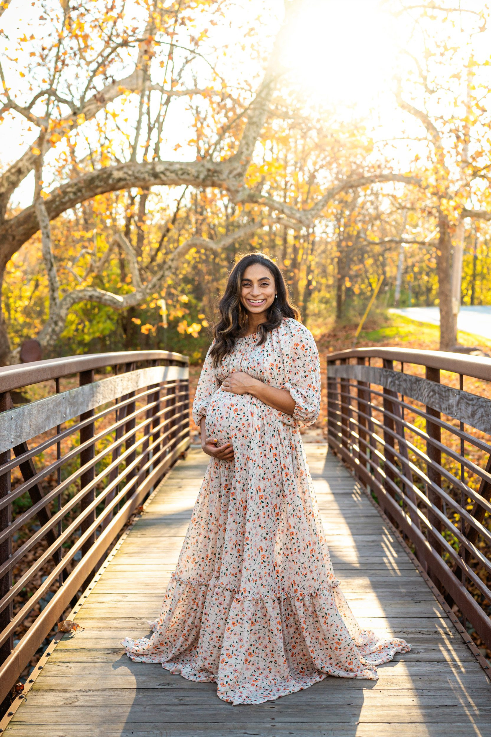 Expecting mother in floral dress on a bridge with fall leaves, second baby, captured at 28 weeks