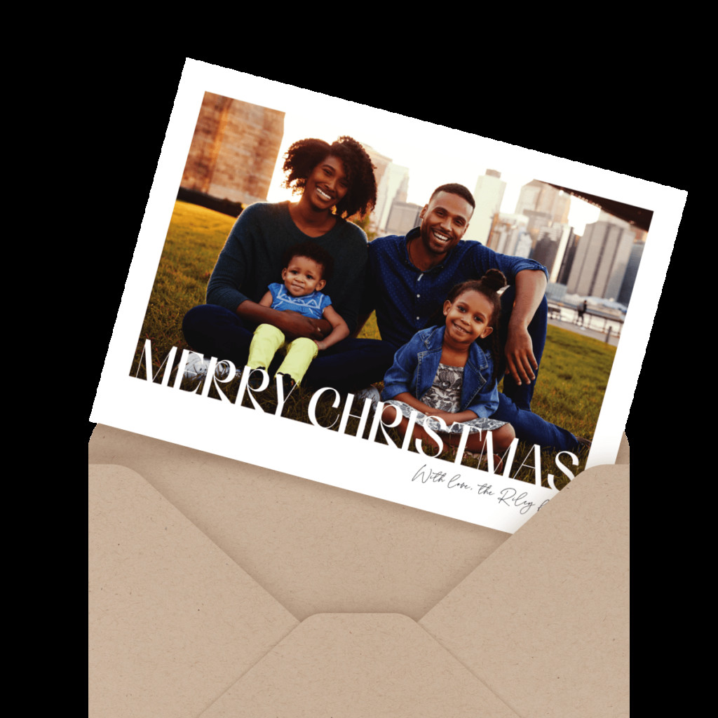 A family of four sitting on grass, smiling. The card says 