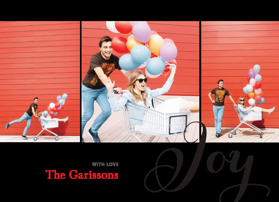 A couple playfully poses with a shopping cart and colorful balloons in front of a red wall.