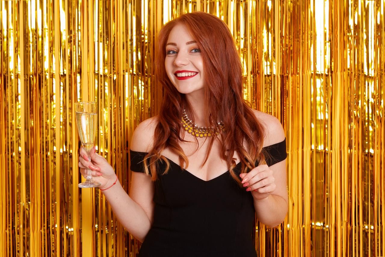 A girl with a glass of wine pose in front of the streamers backdrop.