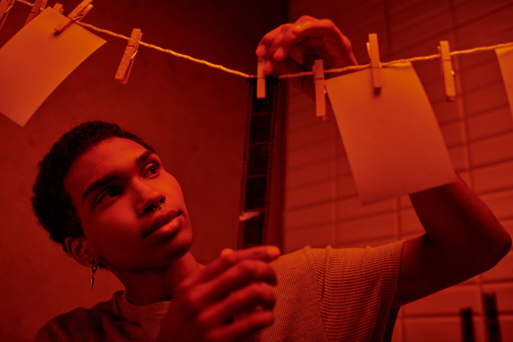 african american photographer hanging up developed film strip in a red lit darkroom