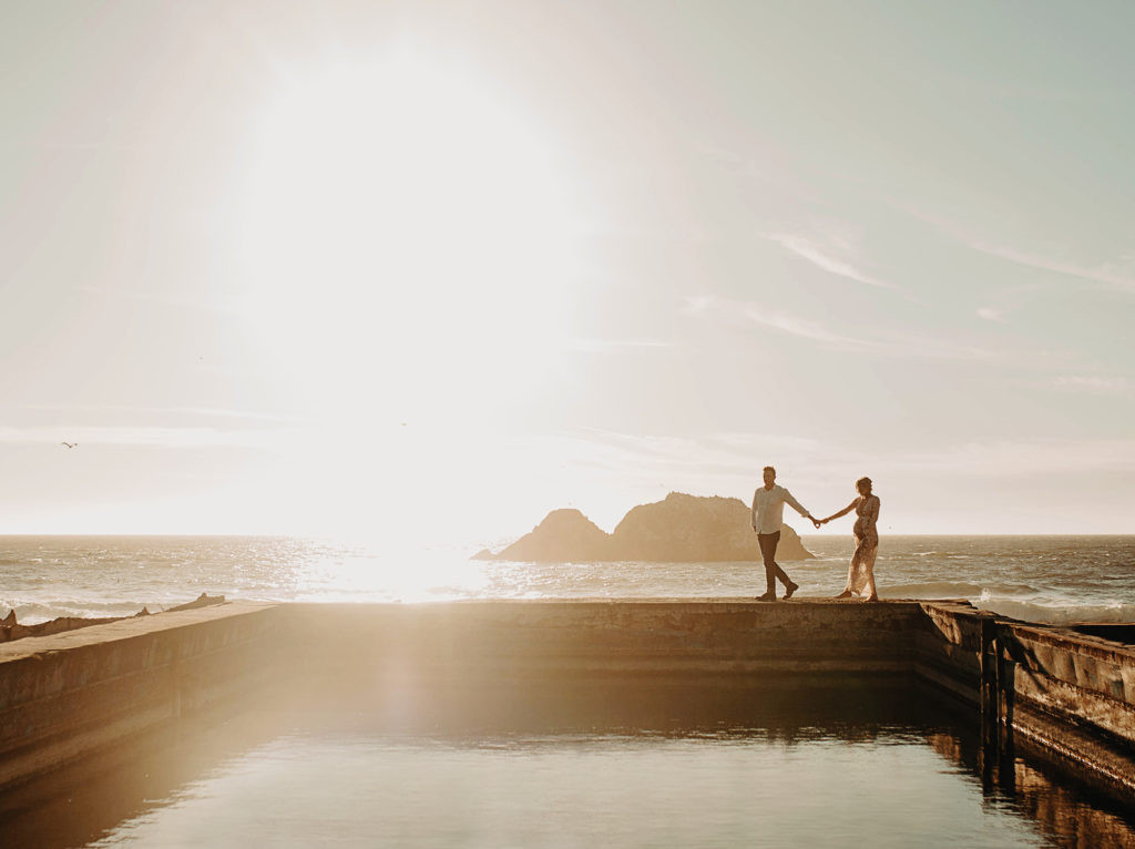 Even in overcast conditions, a couple enjoys a romantic walk by the water, capturing a serene moment.