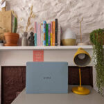 A blue box on a desk next to a yellow lamp. The box contains a digital photo frame