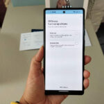 A hand holding a mobile phone. the display shows an app for setting up a digital photo frame