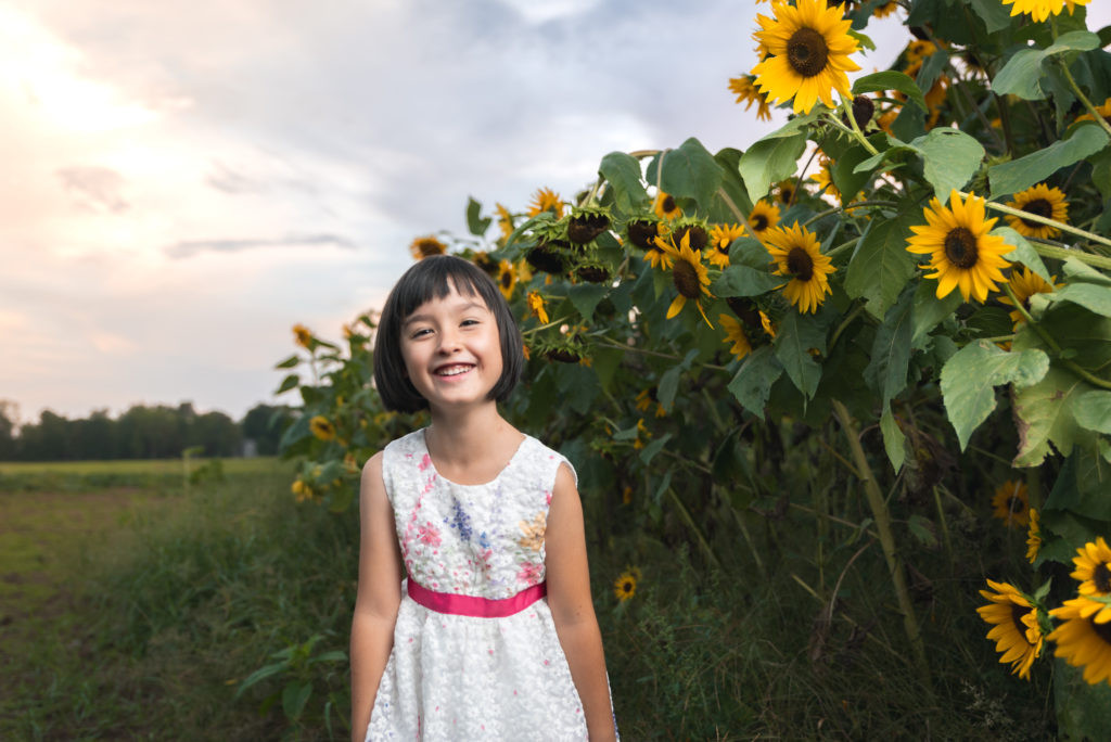 A young girl standing in front of sunflowers.