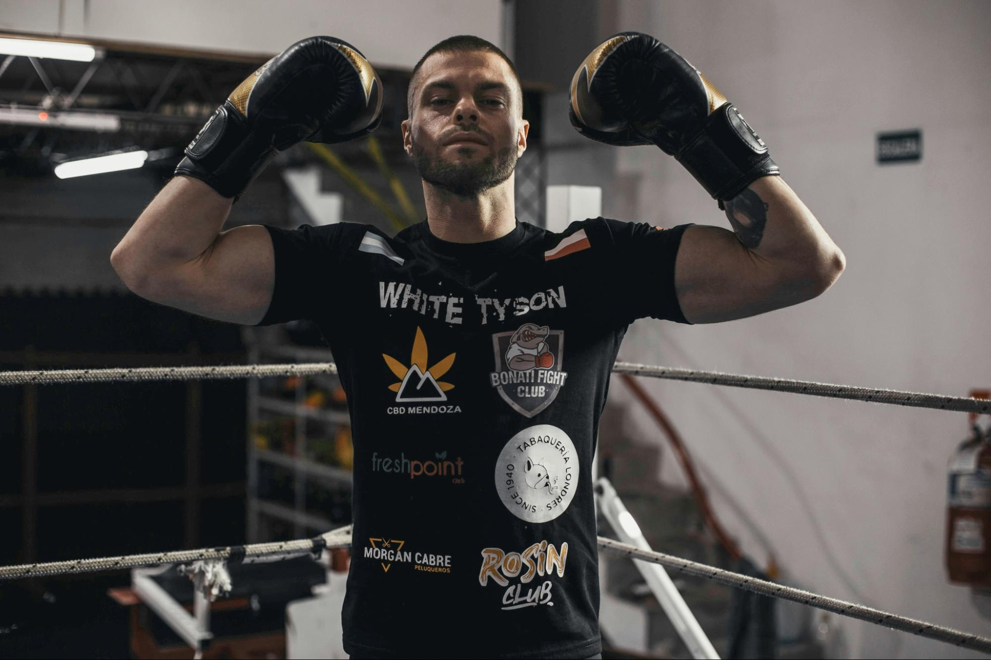 Boxer in ring with sponsor-branded t-shirt, after highlights and shadows adjustment for balanced lighting.