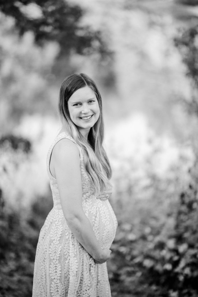 Pregnant woman in a black and white photo, looking down at her belly with hands gently placed on it, soft light emphasizing her form, intimate and tender pose, maternity photography inspiration