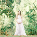 Pregnant woman cradling her baby bump with both hands, standing in a sunlit field, soft focus on her face and hands, baby bump emphasized, natural light, maternity photography inspiration