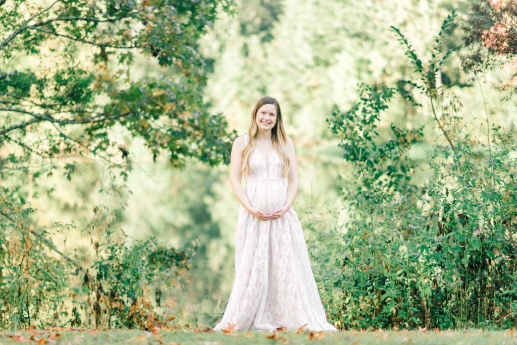 Pregnant woman cradling her baby bump with both hands, standing in a sunlit field, soft focus on her face and hands, baby bump emphasized, natural light, maternity photography inspiration