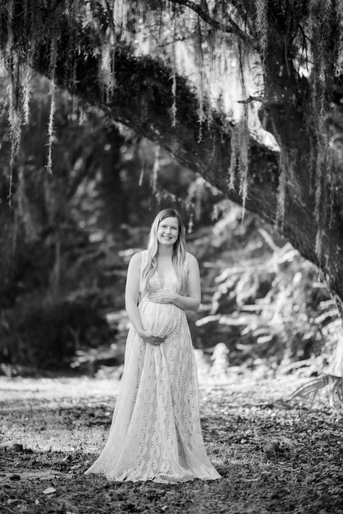 Pregnant woman in a black and white photo, looking down at her belly with hands gently placed on it, soft light emphasizing her form, intimate and tender pose, maternity photography inspiration