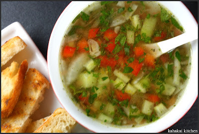 A rustic table setting with a bowl of gazpacho, showcasing the fresh herbs and vegetables used in the dish.