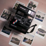 A collection of Polaroid photos displayed on a wall, showcasing their characteristic square format and white borders, with a vintage camera on display.