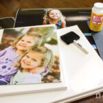 Materials for DIY photo canvas including canvas, photo print, Mod Podge, foam brushes, acrylic paint, and Exacto knife