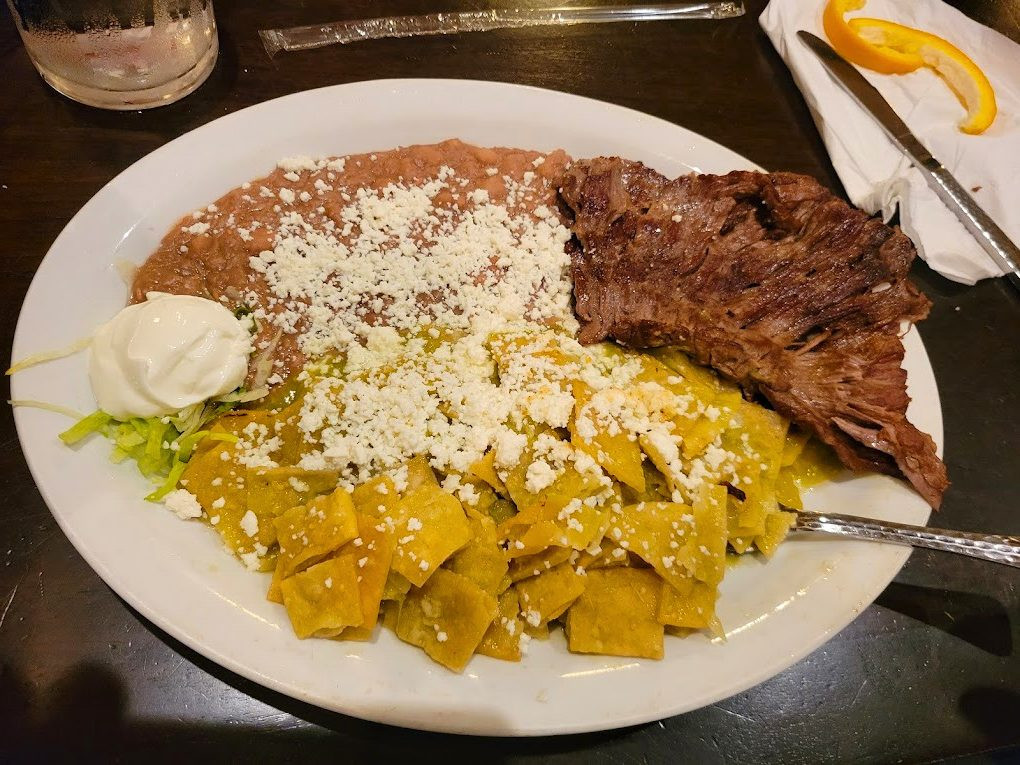 A plate of chilaquiles verdes with grilled steak, beans and sour cream.