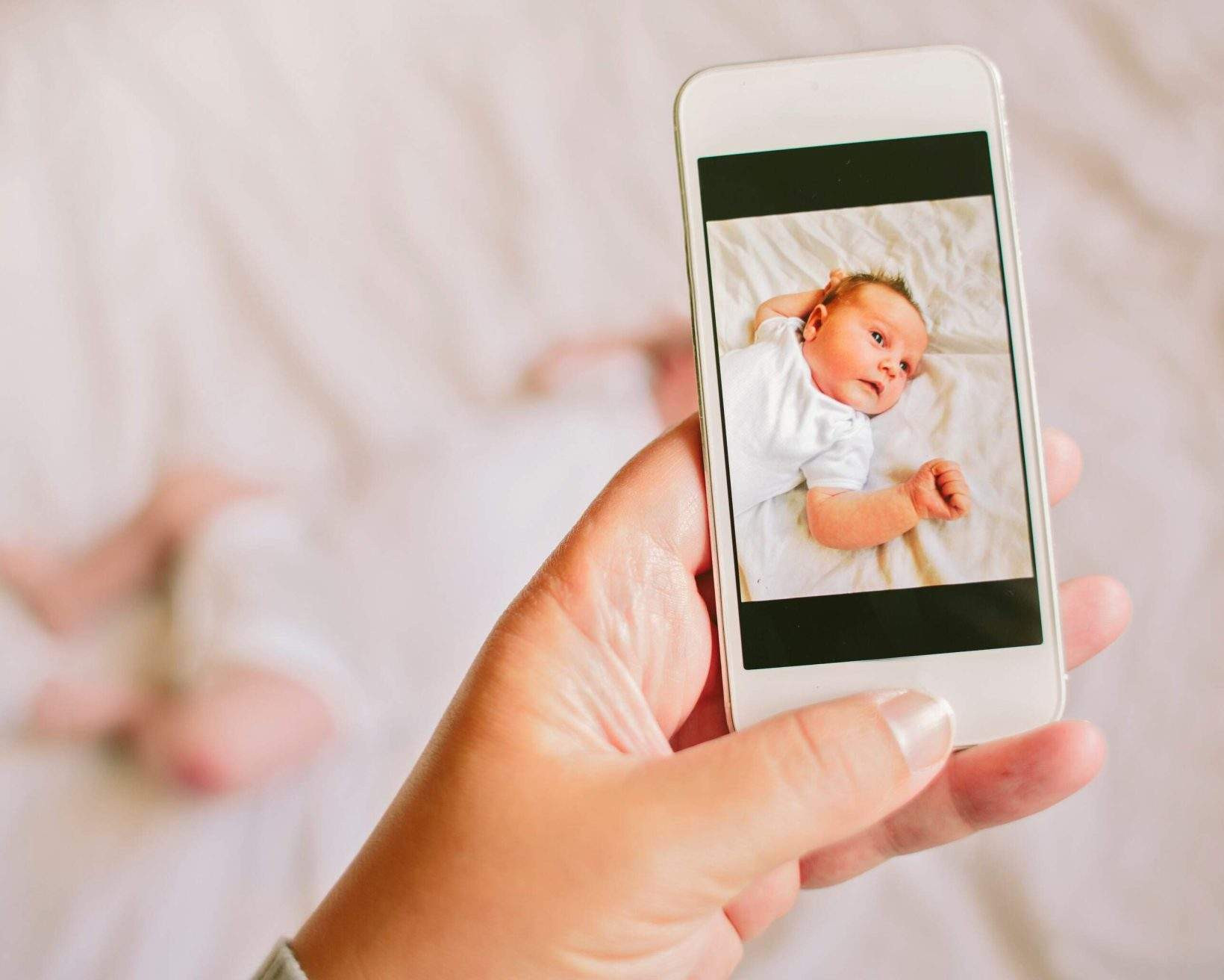 Mother taking a photograph on a smartphone of her newborn baby daughter with a flash
