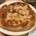 A cong you bing, or scallion pancake, from A&J Restaurant showcasing its flaky layers and savory appeal.